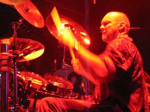 Gary Moffatt striking a cymbal under red lighting