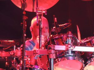 Gary Moffatt at the drums under red concert lights