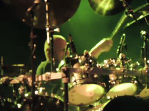 Gary Moffatt performing behind cymbals under green lights
