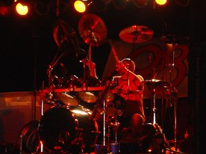 Gary Moffatt playing drums under warm concert lighting