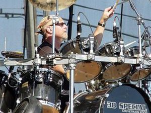 Gary Moffatt raising a drumstick above his outdoor drum kit